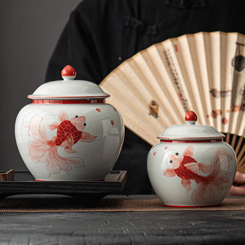 Hand-painted red and blue goldfish ceramic tea caddies displayed on a wooden tray with a traditional folding fan