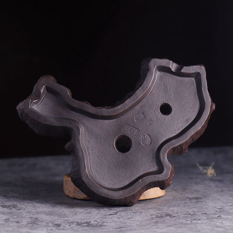 Close up of the underside of a textured brown ceramic bonsai pot showing artisan seals and drainage holes