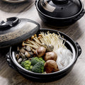 Close up top view of Kuro-Zen ceramic donabe filled with fresh mushrooms, broccoli, and clams on a wooden table