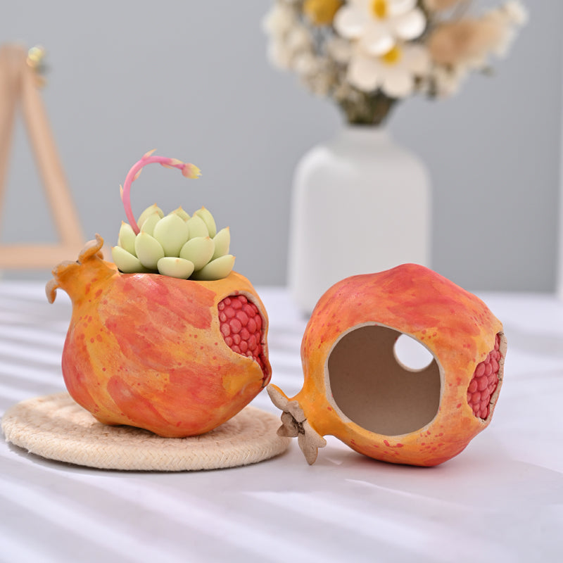 Handcrafted pomegranate shaped ceramic planter with a small succulent placed on a white table with soft shadows