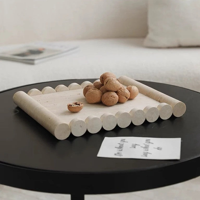 Scalloped travertine stone sculptural tray featuring walnuts on a black minimalist coffee table