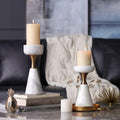 Lifestyle shot of two marble and brass candle holders with lit pillar candles on a coffee table with books