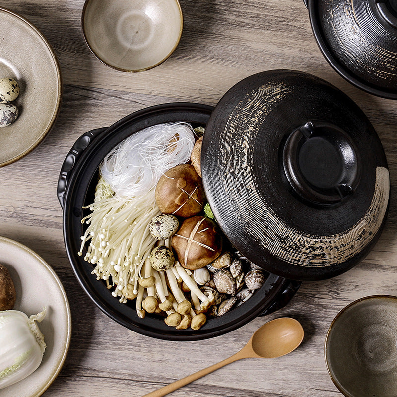 Top down lifestyle shot of black handcrafted clay pot surrounded by ceramic bowls and wooden spoon
