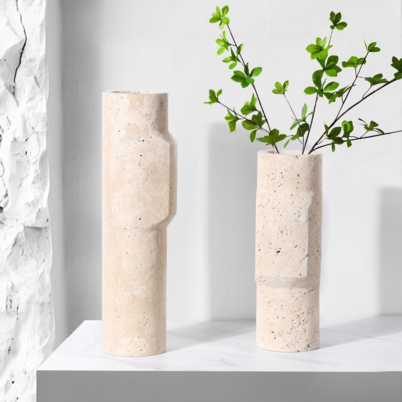 A tall and a medium sized cylindrical travertine stone vase with geometric details and green branches