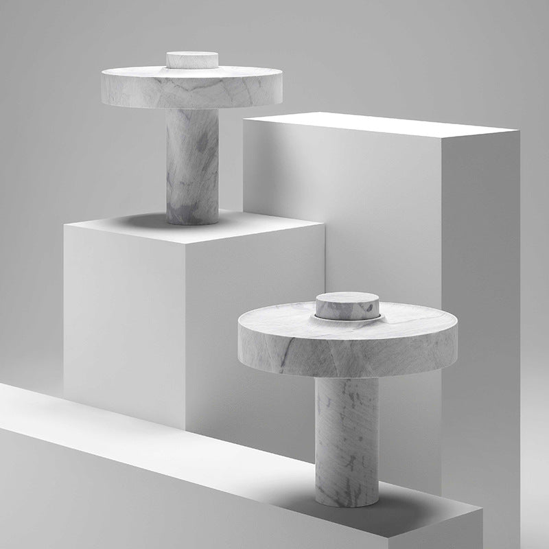 A pair of modern marble table lamps with flat disc shades arranged on geometric white blocks in a studio setting