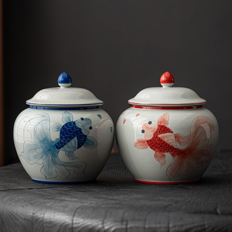 Pair of white porcelain storage jars featuring artisanal red and blue goldfish illustrations side by side