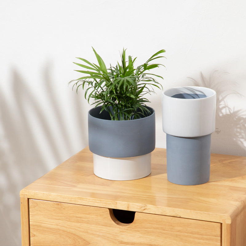 Modern geometric ceramic planters in slate and bone white sitting on a light wood dresser with a green parlor palm