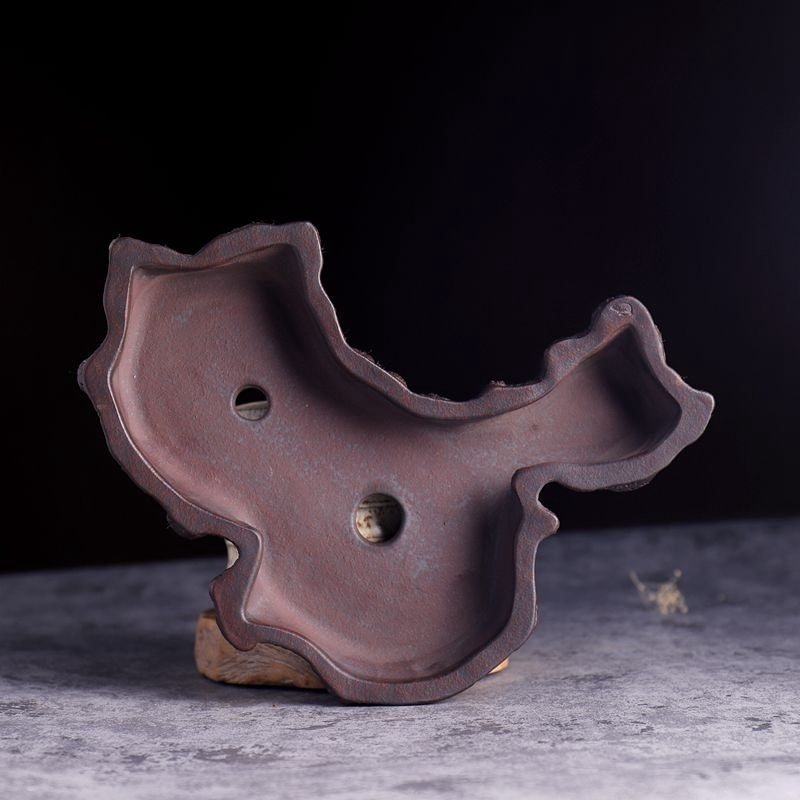 Top down view of a free-form organic shaped brown clay bonsai planter with two drainage holes