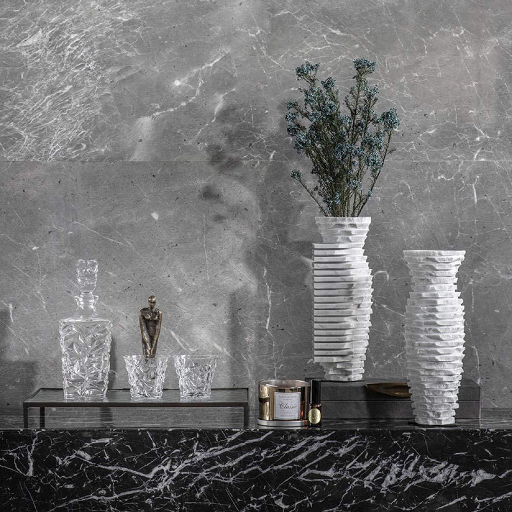 A set of two sculptural stone vases with horizontal layered texture displayed against a grey marble wall with crystal decanters