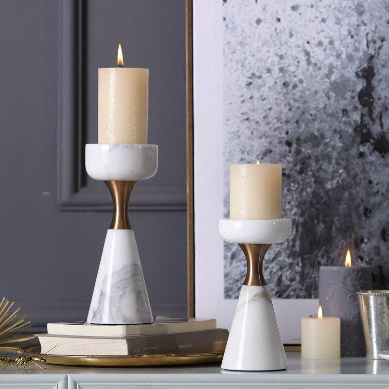 Close up of luxury marble candle holders on a grey sideboard next to framed art and smaller candles