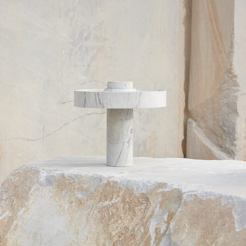 A single white marble table lamp placed on a raw stone block in a marble quarry representing material honesty