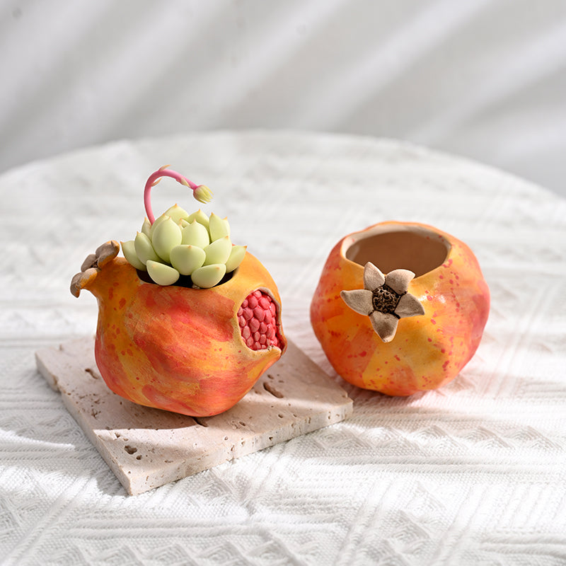 Close up of a pomegranate ceramic planter with realistic seed details resting on a stone tile