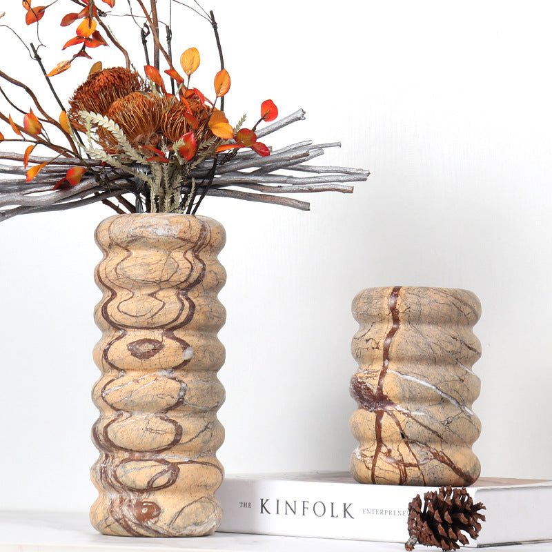 Close up of a large ribbed marble vase holding dried orange leaves and silver branches on a marble surface