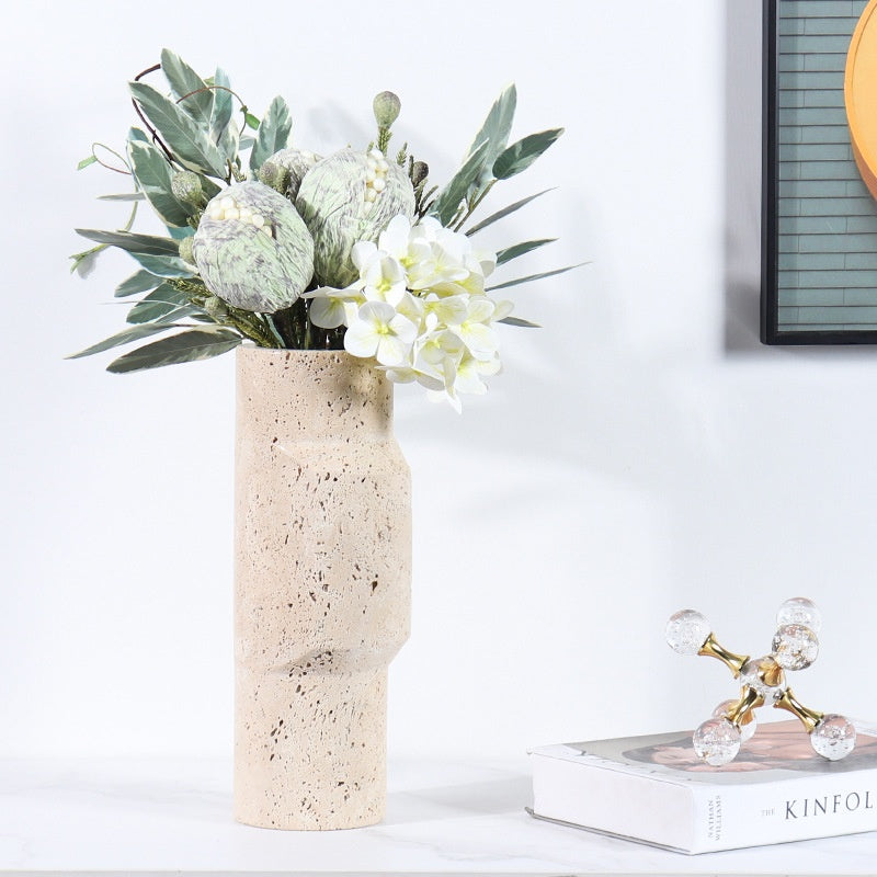 Close up of a travertine stone sculptural vase holding a lush arrangement of white plumeria and green leaves