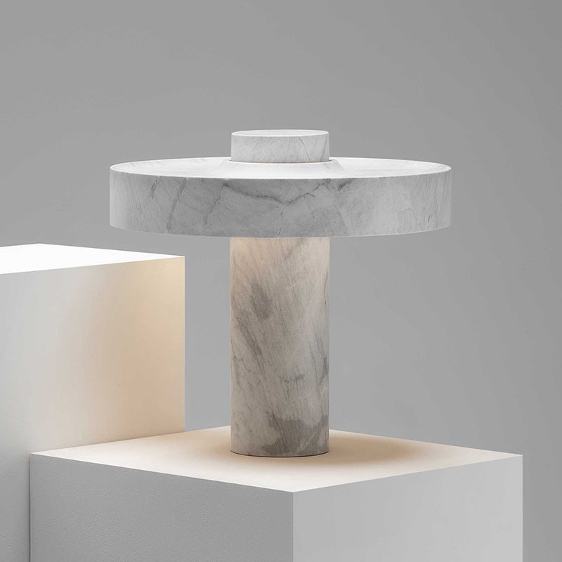 Close up view of a handcrafted marble table lamp showing the detailed grey veining and the warm light reflecting on a white surface