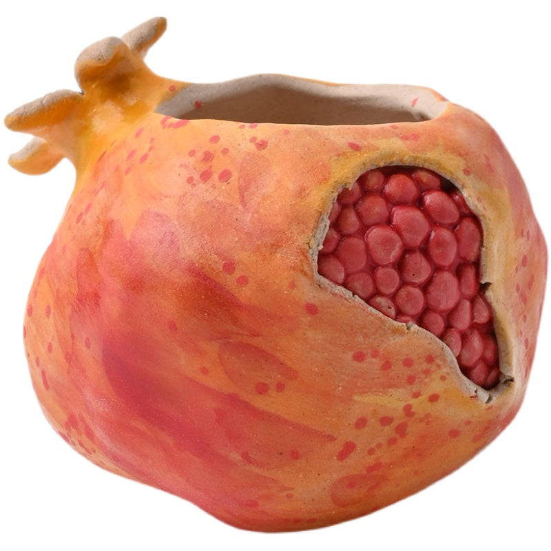 Studio shot of a pomegranate ceramic planter showing the intricate hand carved red seed cluster and textured glaze