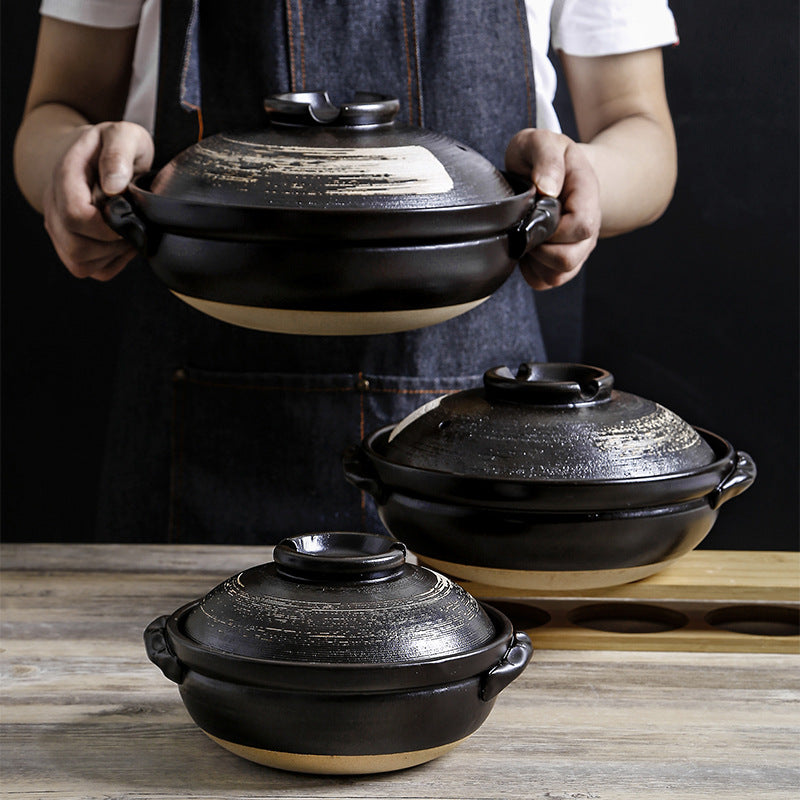 Person in apron holding a large Kuro-Zen clay pot next to two smaller sized matching pots