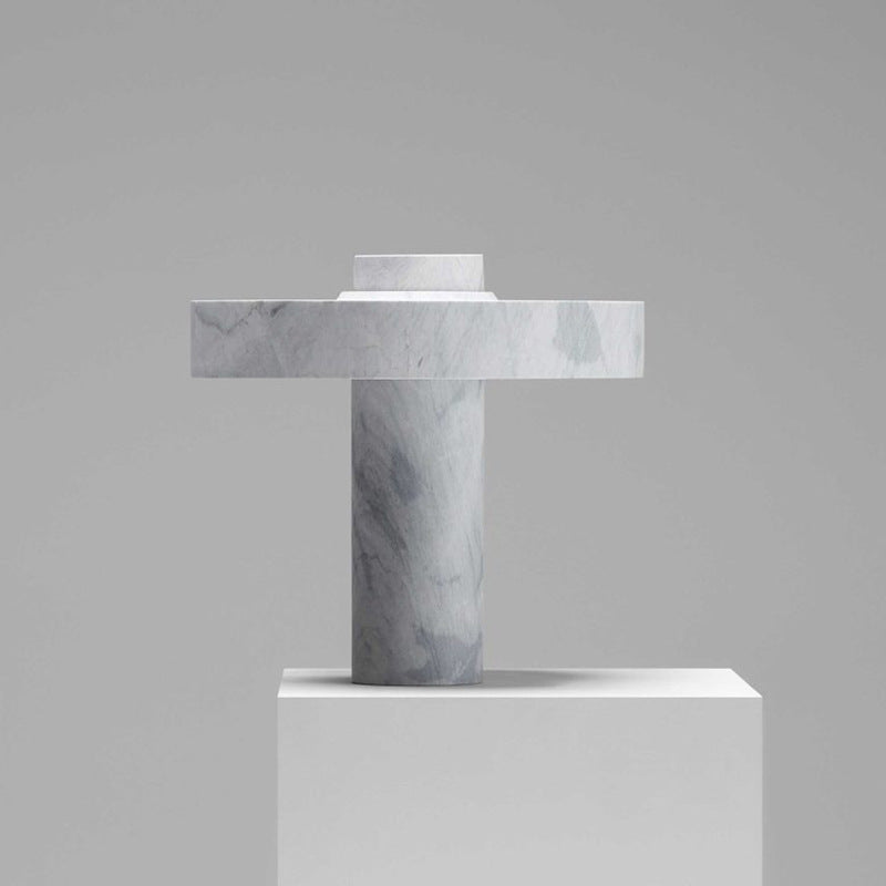 Front perspective of a circular marble table lamp with a thick pillar base against a neutral grey background