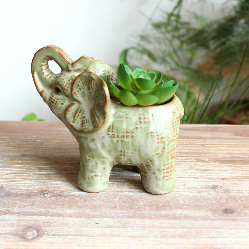 Sage green ceramic elephant planter with trunk raised holding a lush green succulent