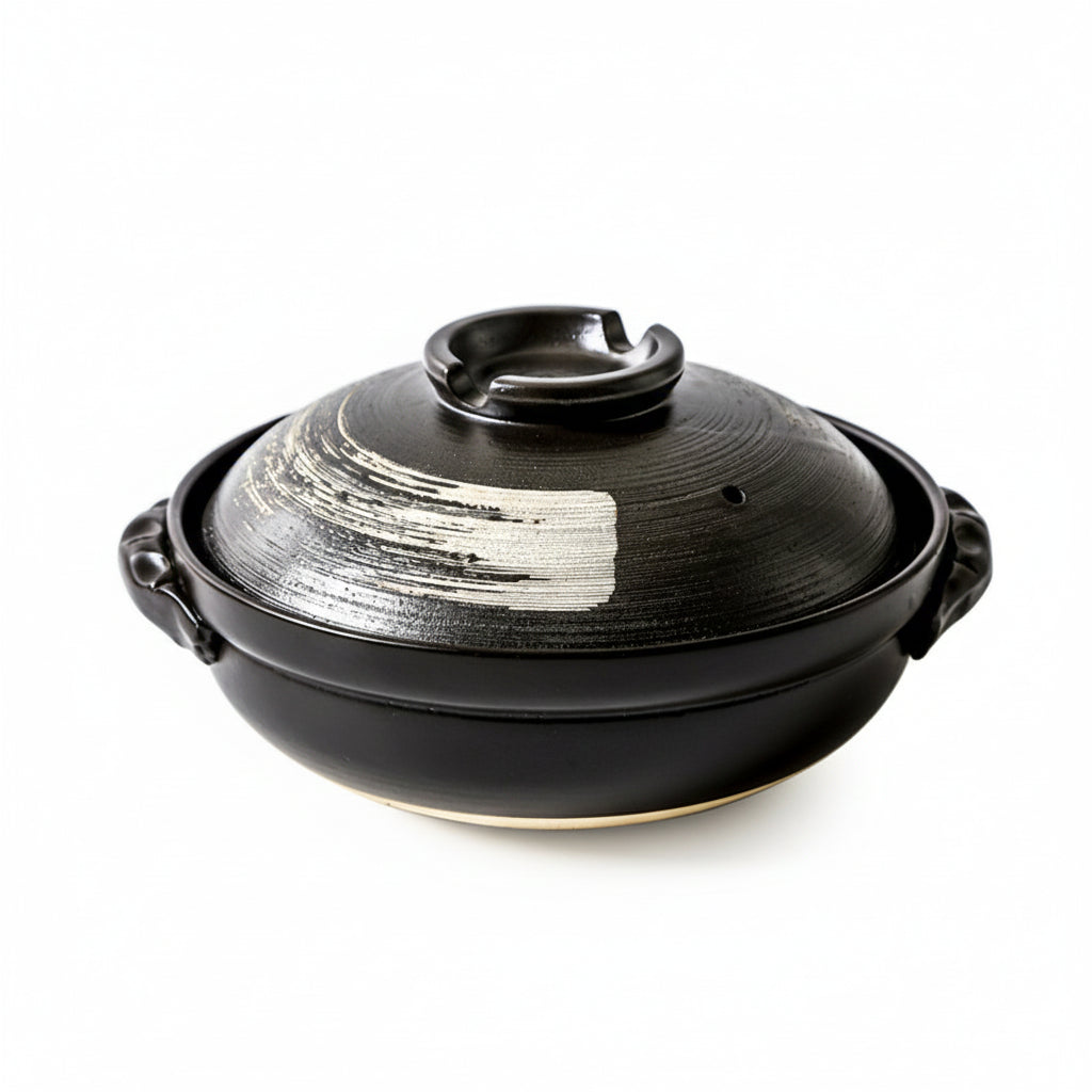 Studio shot of a black ceramic donabe with white hand-painted brushstroke against a white background