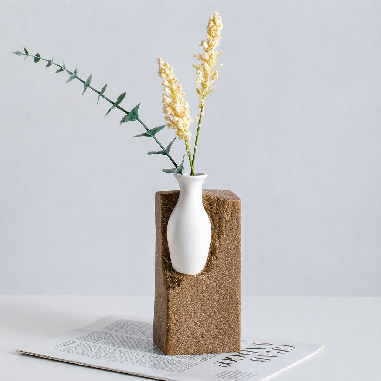 Tall brown abstract ceramic vase styled with cream flowers and greenery