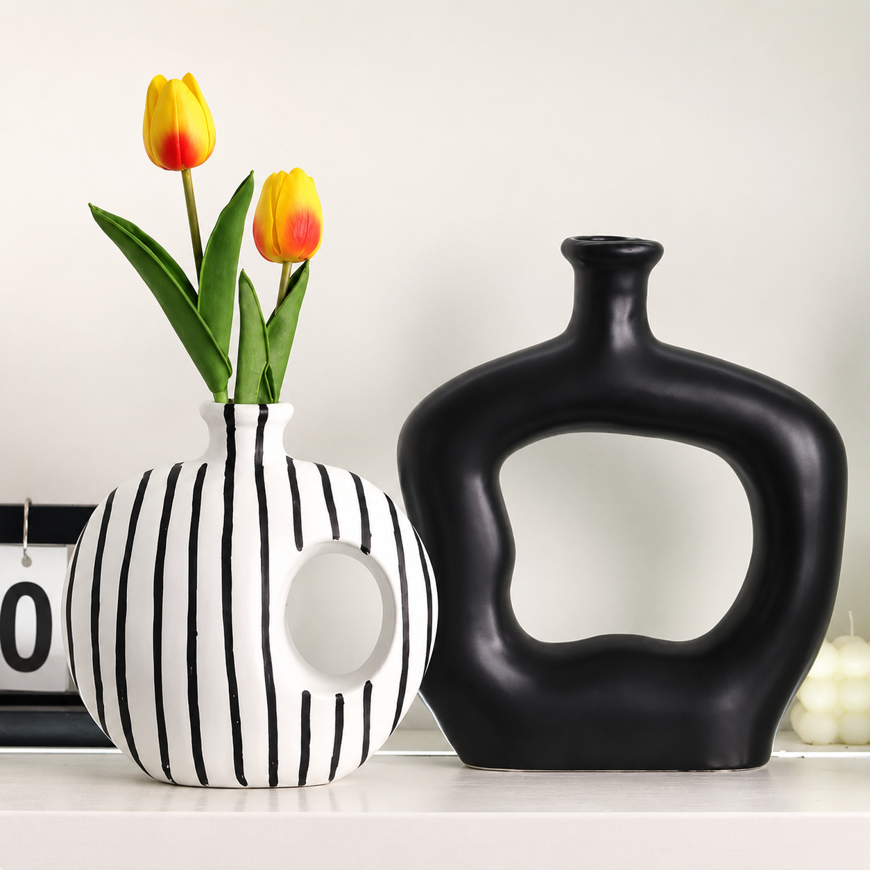 Black and white striped vase beside matte black hollow ceramic vase