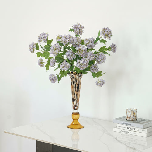 Amber glass vase with purple flowers on white tabletop for elegant home decor