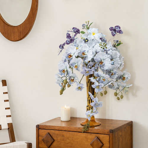 Amber glass vase with blue orchid arrangement on wooden cabinet