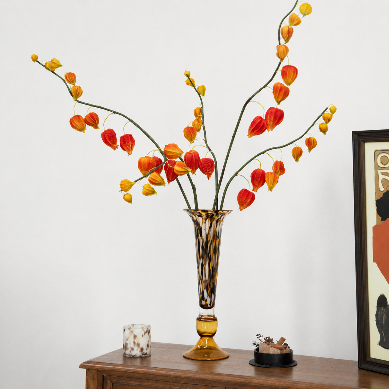 Amber glass vase with orange stems on wooden sideboard