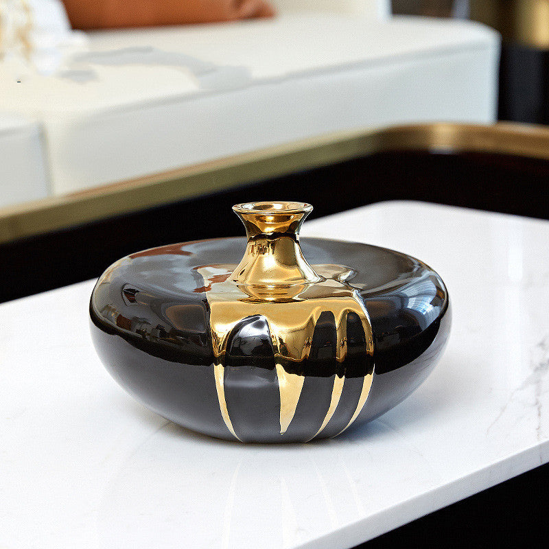 Short black ceramic vase with gold drip accents on modern tabletop