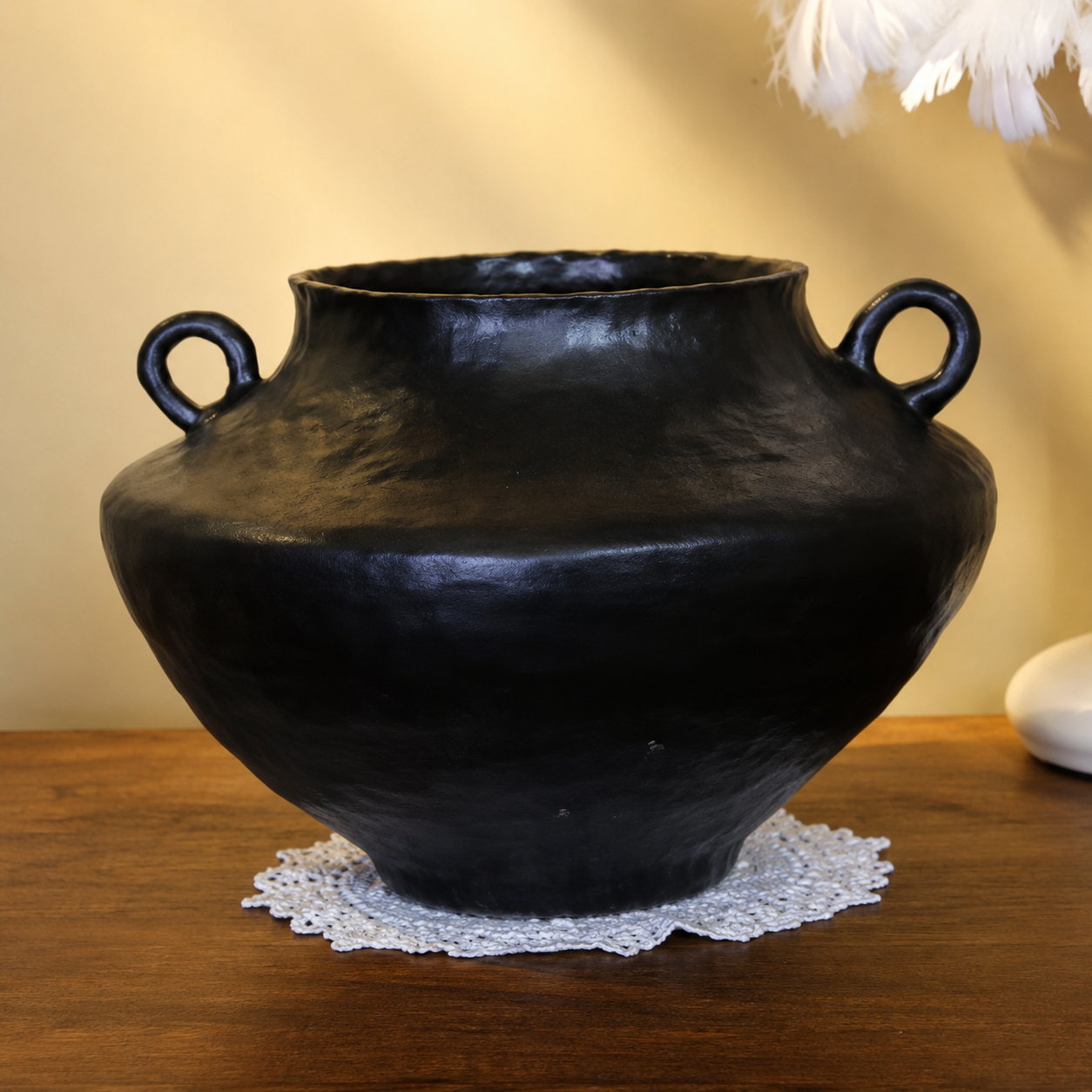 Black rustic ceramic vase with handles displayed on a wooden table under warm lighting
