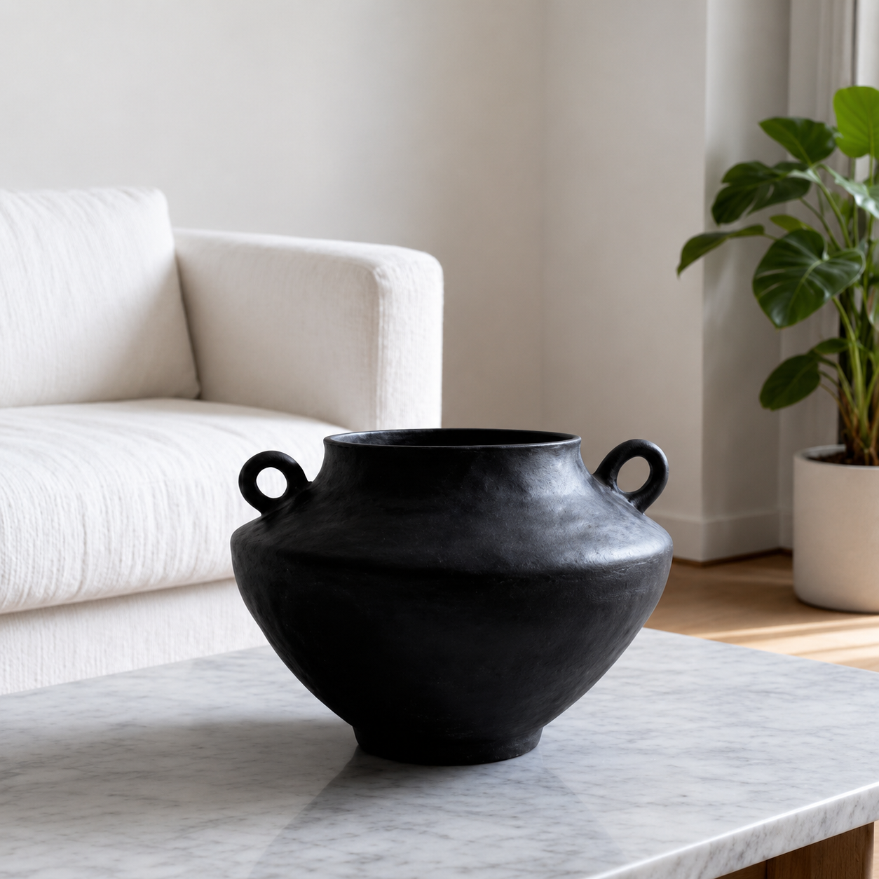 Black rustic ceramic vase with handles styled on a marble coffee table in a neutral living room