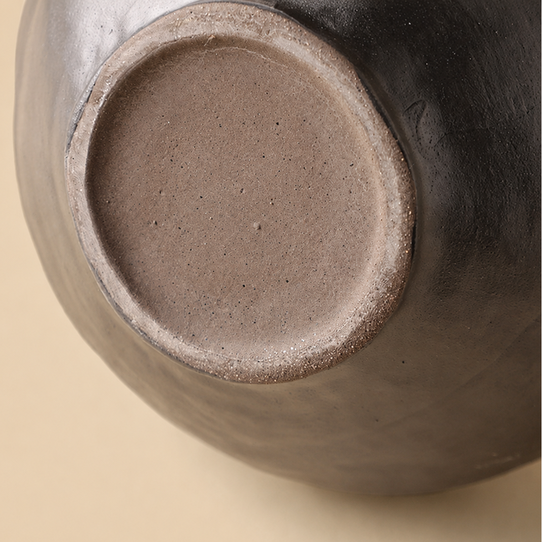 Close up of black ceramic vase base showing unglazed ceramic foot and artisanal texture
