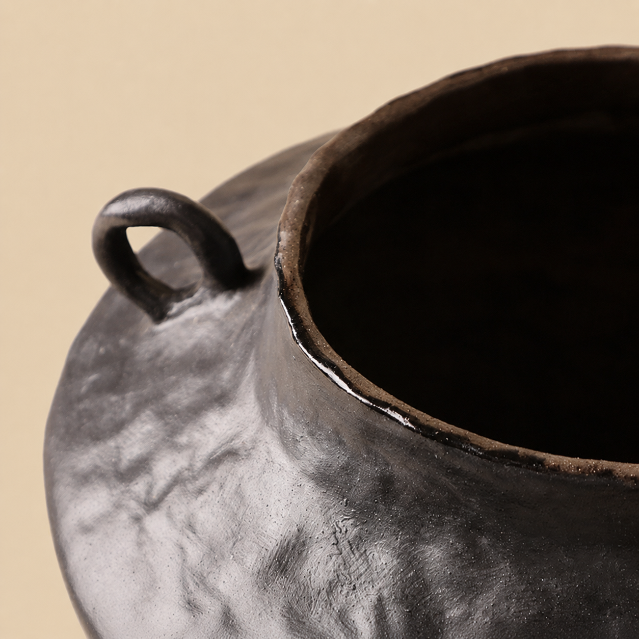 Close up of black ceramic vase rim and handle showing handmade rustic finish