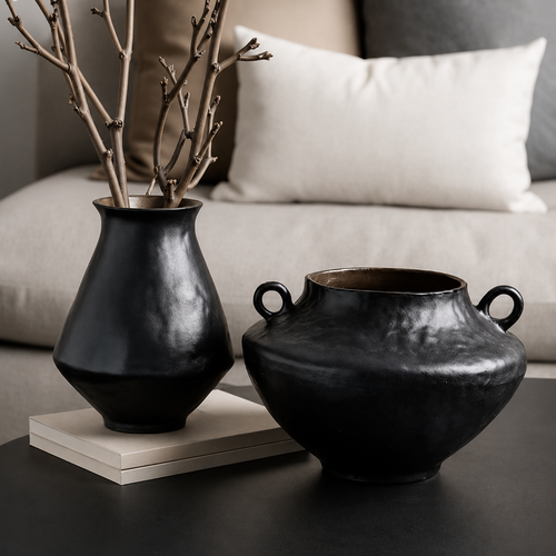 Black ceramic vase with handles styled beside a tall vase with branches on a modern coffee table