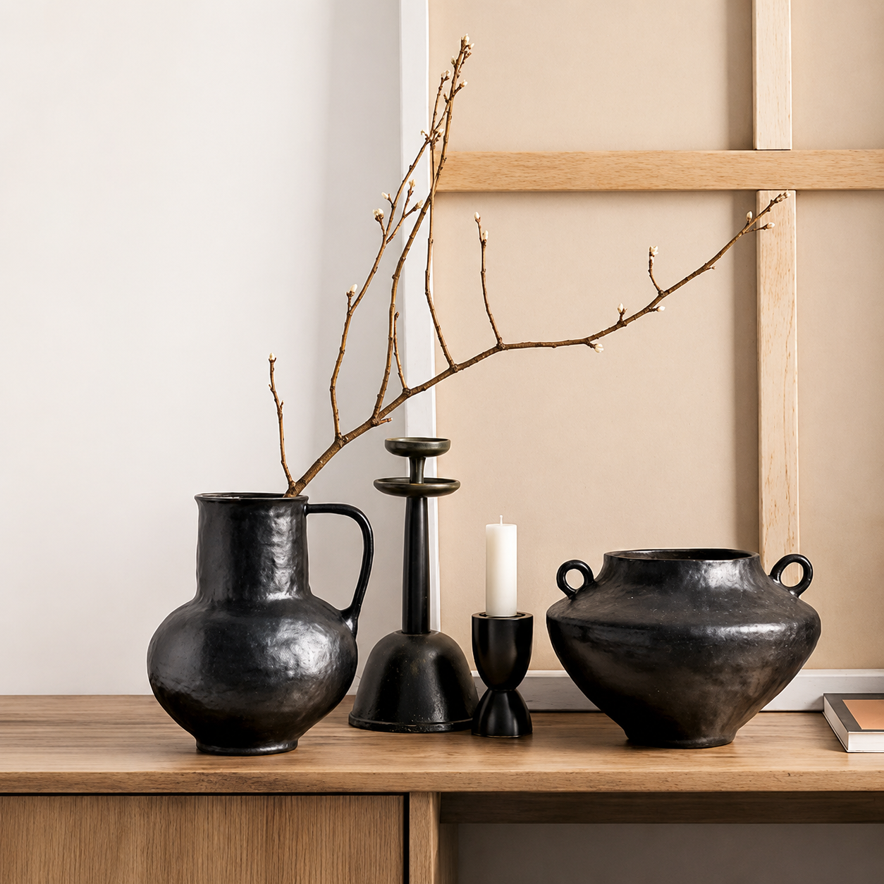 Black rustic ceramic vase with handles displayed with candle holders and branches on a wooden console
