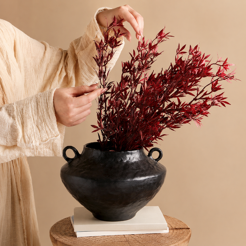 Black rustic ceramic vase with handles styled with red foliage on a neutral side table