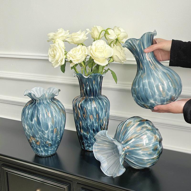 Blue art glass vases with ruffled rims styled with white flowers on black console table