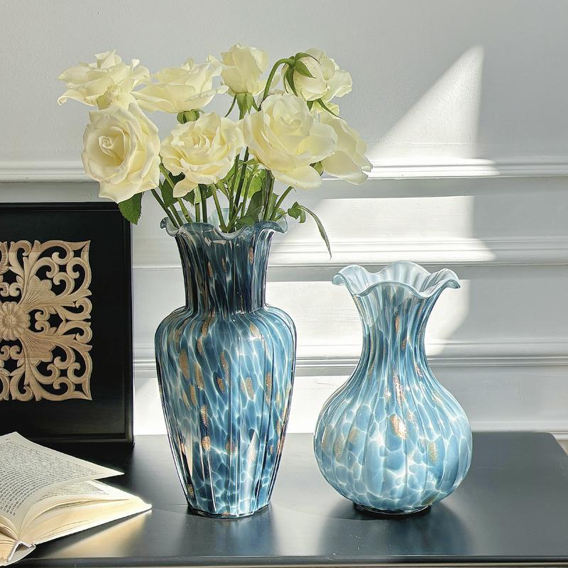 Blue art glass vase with ruffled rim styled with white roses beside matching vase