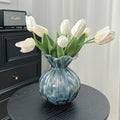Blue ruffled art glass vase with white tulips on black round table