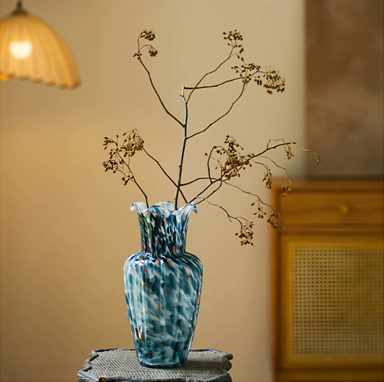 Tall blue art glass vase with dried branches on warm interior side table