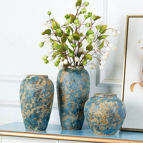 Blue gold textured ceramic vases arranged with leafy branches on a decorative console table
