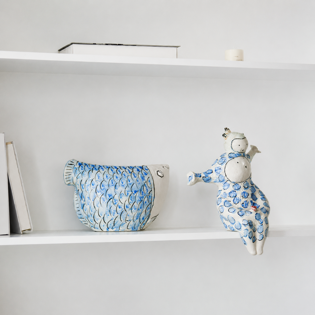 Blue and white ceramic fish vase displayed on white shelf beside matching decorative figurine