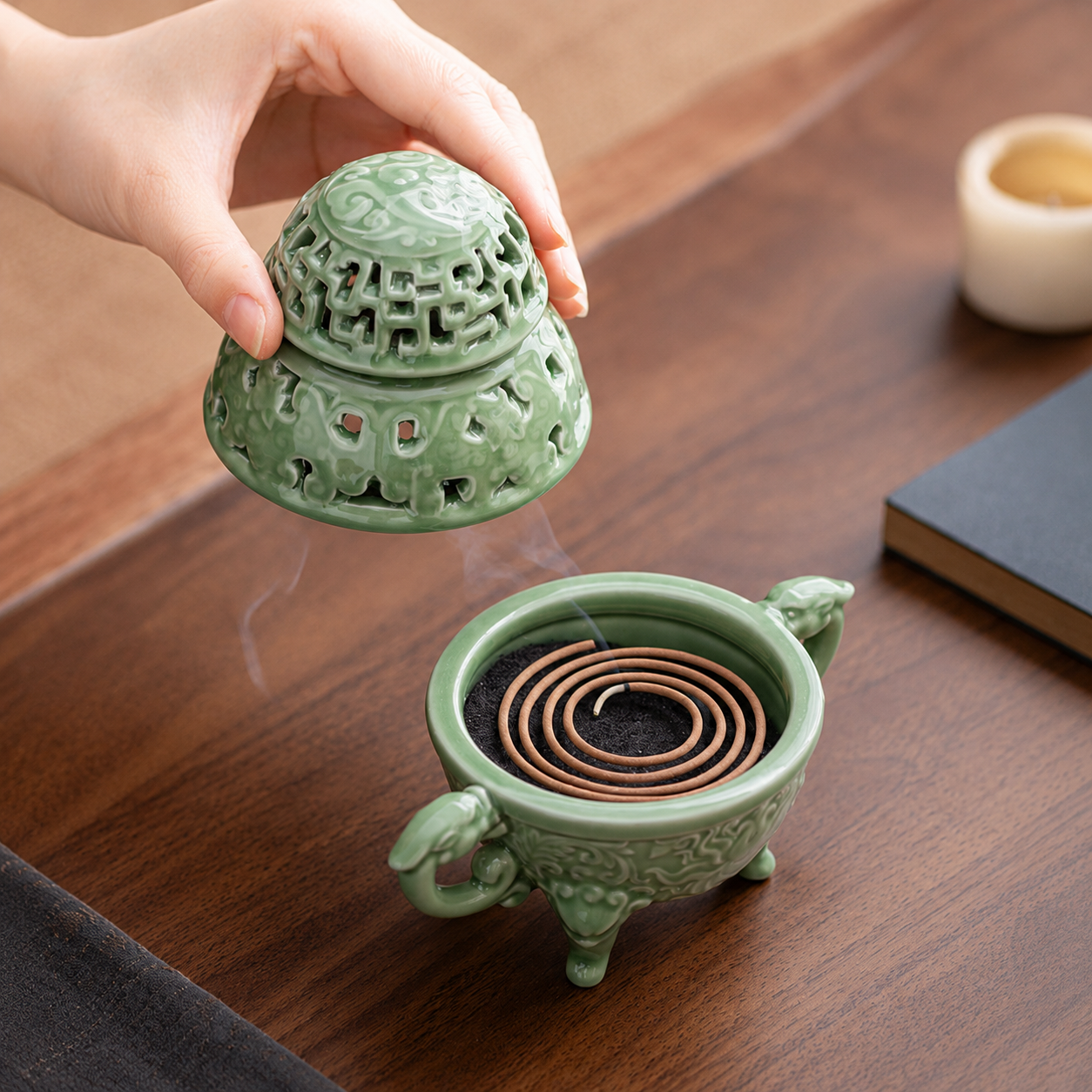 Hand lifting the lid of a celadon green ceramic incense burner to reveal an incense coil inside