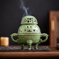 Celadon green ceramic incense burner with smoke rising on a dark tabletop