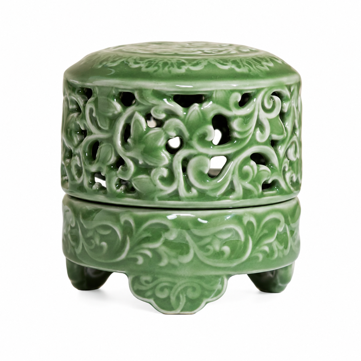 Carved celadon green ceramic incense burner with pierced sides and three feet on white background