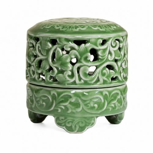 Carved celadon green ceramic incense burner with pierced sides and three feet on white background