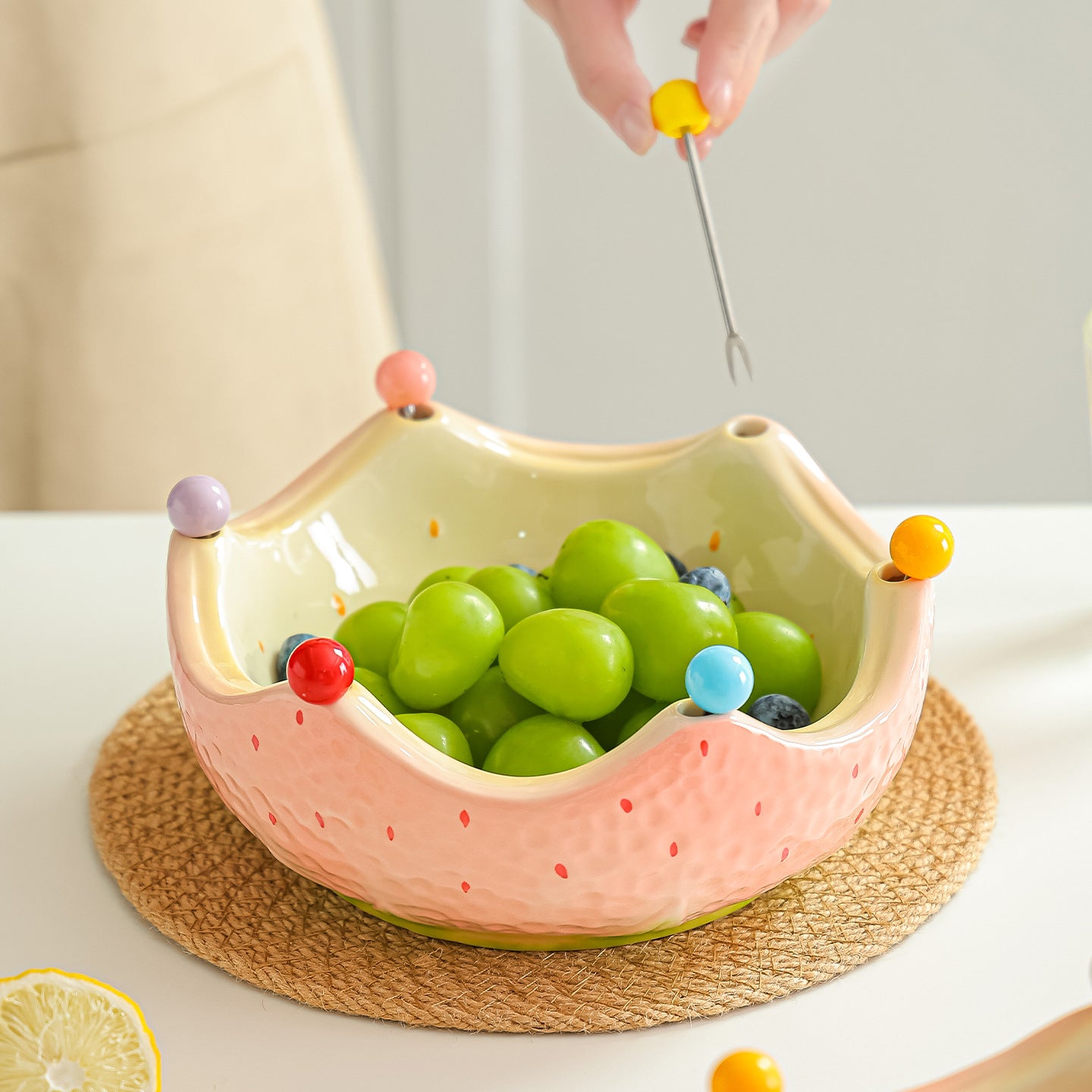 Pink ceramic crown fruit bowl filled with green grapes on a woven placemat