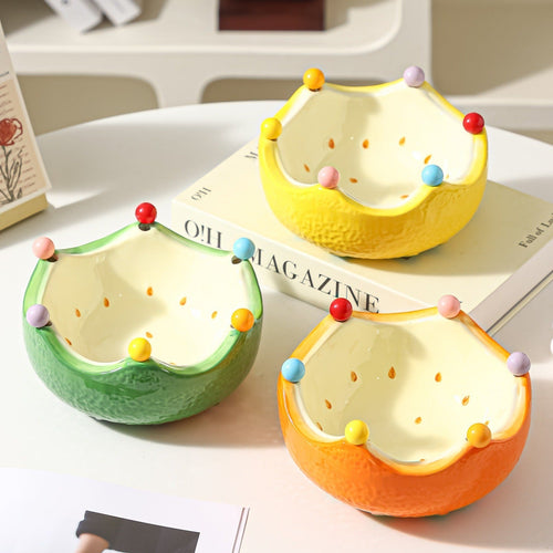 Colorful ceramic crown fruit bowls in yellow green and orange displayed together on a table