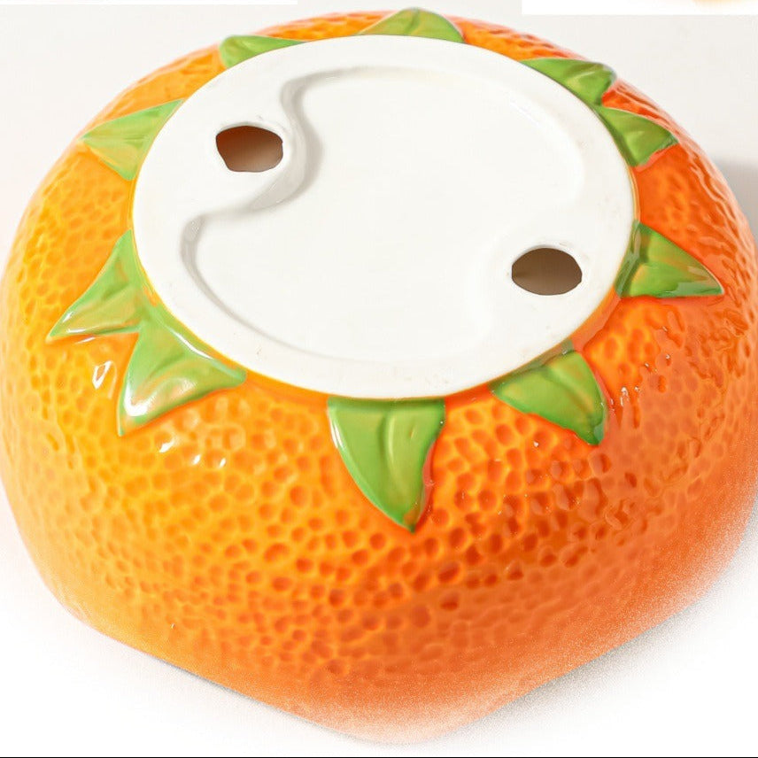 Bottom view of orange ceramic crown fruit bowl showing raised foot and painted green leaf details